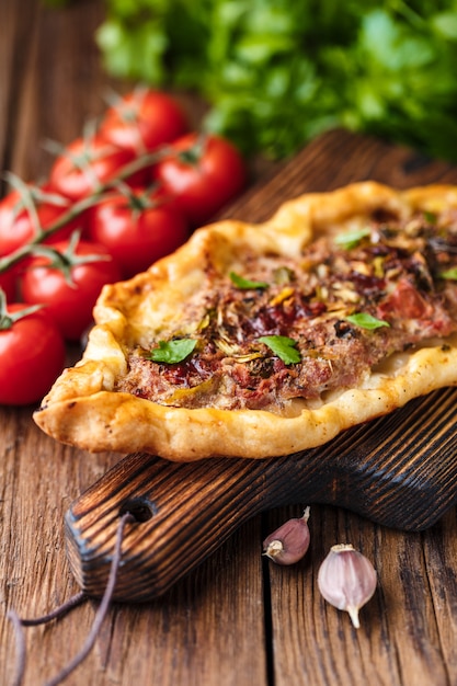 Pide casalingo turco su una tavola di legno marrone rustica. pomodorini, prezzemolo, peperoncino piccante, aglio sono sul tavolo.