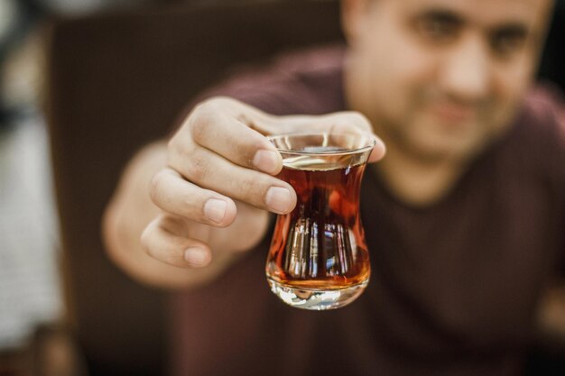 Foto un uomo turco tiene il tè nero in un bicchiere tradizionale