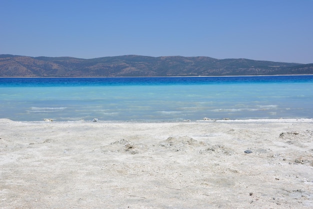 турецкое горное озеро Салда с голубой водой и белым песком в жаркий солнечный день