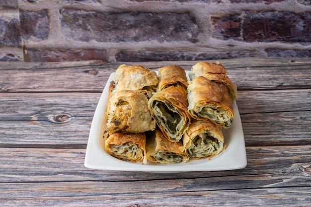 Turkish pastry with spinach and cheese on a white plate. A traditional Turkish pastry, roll pastry. Spinach and cheese pie on a wooden table.