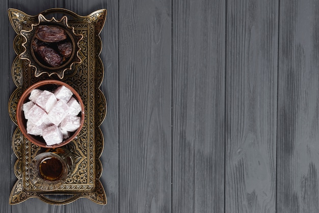 Turkish ramadan dessert lukum; tea and dates on engraved metallic tray over the black wooden surface