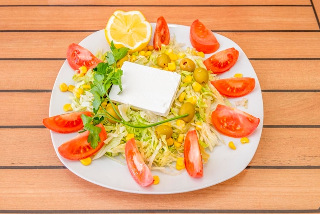 Turkish salad with fresh square cheese sweet corn iceberg lettuce with lots of tomato wedges pitted Spanish olives and a sprig of parsley