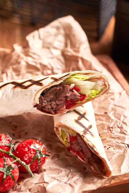 Turkish Shawarma with beef and fried with tomatoes on craft paper on wooden plate Fast food set Close up view