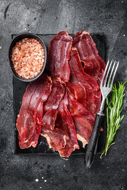 Turkish sliced pastrami kayseri pastirma dried beef meat with\
spices on marble board black background top view