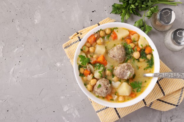 Photo turkish soup with chickpeas, meatballs and vegetables in a white bowl on a gray background