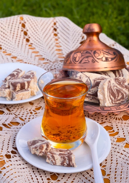 Turkish tea in a glass Cup and marble halva on a table with a handmade tablecloth and candy maker