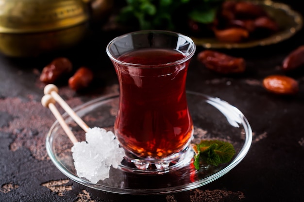 Турецкий чай в традиционной стеклянной чашке с карамелизированным сахаром и мятой на темном фоне