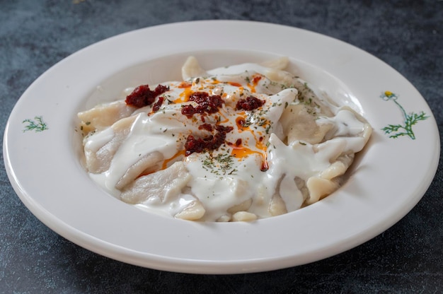 Традиционные турецкие равиоли с йогуртом и томатным соусом на тарелке манти