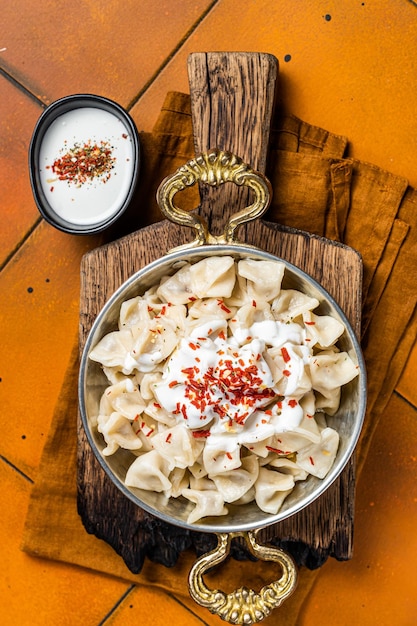 Turkse traditionele manti met yoghurt en tomatensaus in een koekenpan Oranje achtergrond Bovenaanzicht