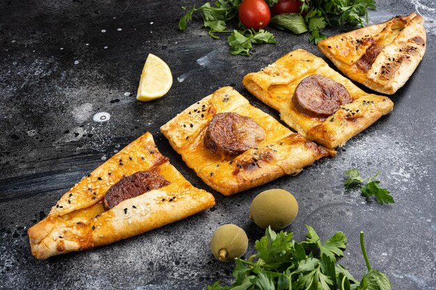 Foto turkse traditionele sucuklu pide met pepperoni op zwarte donkere stenen tafelondergrond