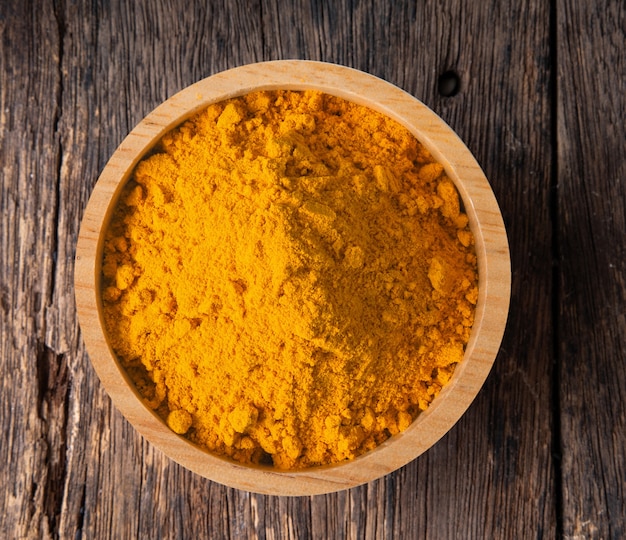 Photo turmeric (curcuma) powder pile in wood bowl