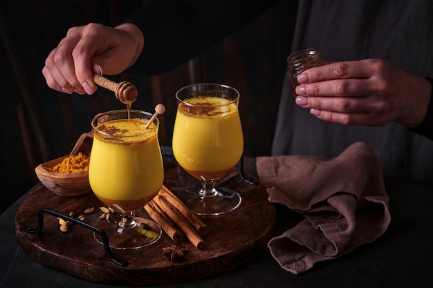 Turmeric golden milk latte with cinnamon sticks and honey. Healthy ayurvedic drink. Trendy Asian natural detox beverage with spices for vegans. Copy space.