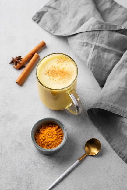 Foto latte al latte dorato alla curcuma con spezie e miele detox che aumenta l'immunità in una tazza di vetro su uno sfondo chiaro