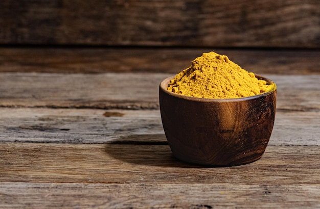 Turmeric, an oriental spice, in a wooden bowl on a wooden table.