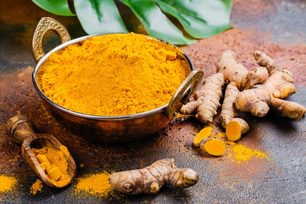 Turmeric powder and fresh root on grunge background