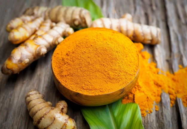 Turmeric powder and fresh turemric in wood bowls on wooden table. Herbs are native to Southeast Asia.