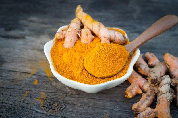 Turmeric powder and fresh turmeric in white bowls on old wooden table. herbal