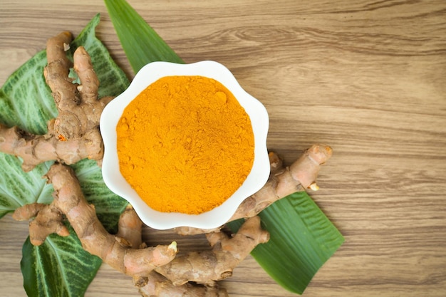 Polvere di curcuma e curcuma fresca con foglia verde in ciotole bianche su tavola di legno a base di erbe