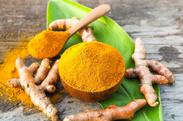 Turmeric powder and fresh turmeric in wood bowl on wooden table. Herbs