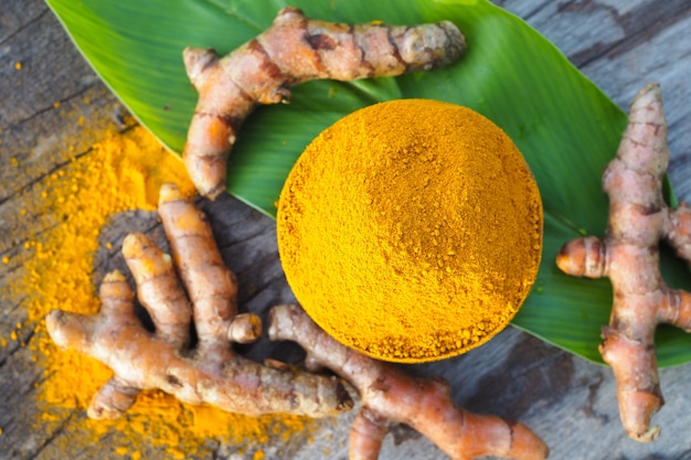 Turmeric powder and fresh turmeric in wooden bowls on old wooden table