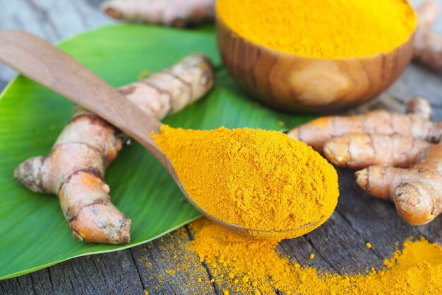 Polvere di curcuma e curcuma fresca in cucchiaio di legno e curcuma fresca sulla vecchia tavola di legno