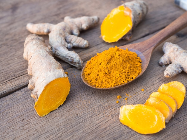 Turmeric powder and fresh turmeric in wooden spoon with green leaf on old wooden table. 