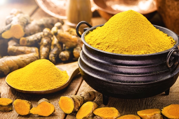 Turmeric powder in molten metal bowls on wooden table, spices, turmeric, turmeric root