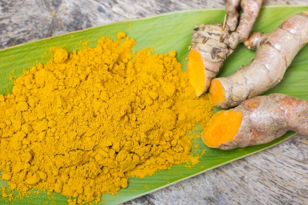 Turmeric powder roots and leaf curcumin herb on wooden table