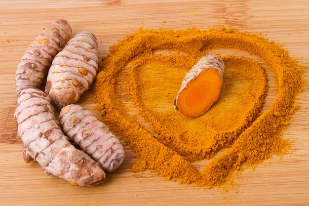 Turmeric powder and roots on wooden background