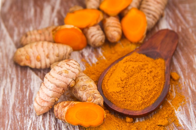 Turmeric powder and roots on wooden background