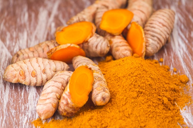 Turmeric powder and roots on wooden background