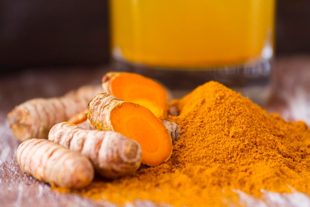 Turmeric powder and roots on wooden background