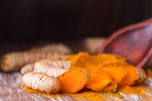 Turmeric powder and roots on wooden background