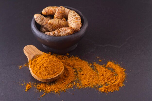 Turmeric powder and roots on wooden background