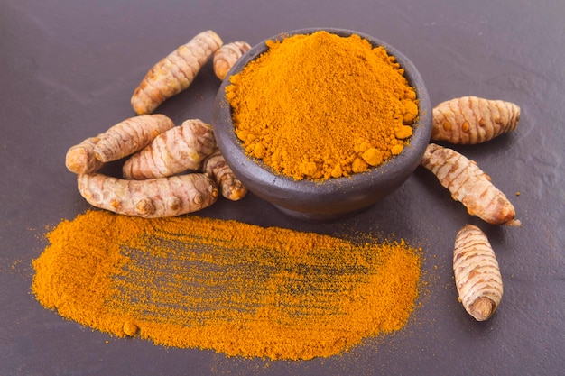 Turmeric powder and roots on wooden background