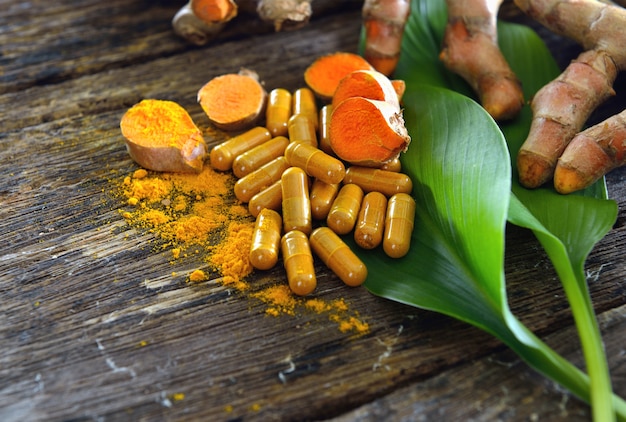 Turmeric powder and turmeric capsules on wooden surface