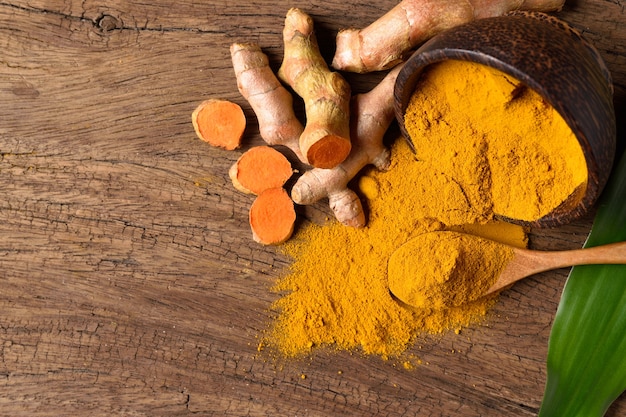 Photo turmeric powder in wooden bowl and spoon with fresh rhizome