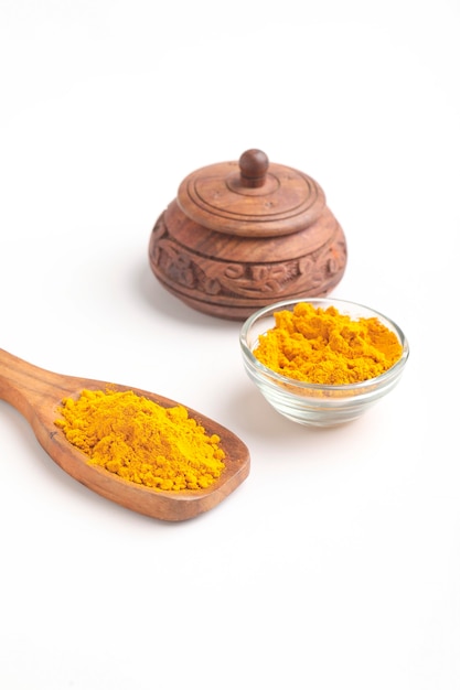 Turmeric powder in wooden spoon and glass bowl on white surface