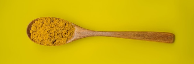 Polvere di curcuma in un cucchiaio di legno su uno sfondo giallo banner formato lungo