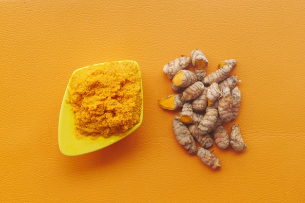 Turmeric root and paste in a bowl on orange background