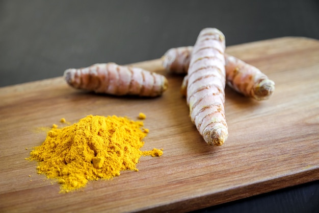 Radice di curcuma e polvere di spezie su un tagliere di legno