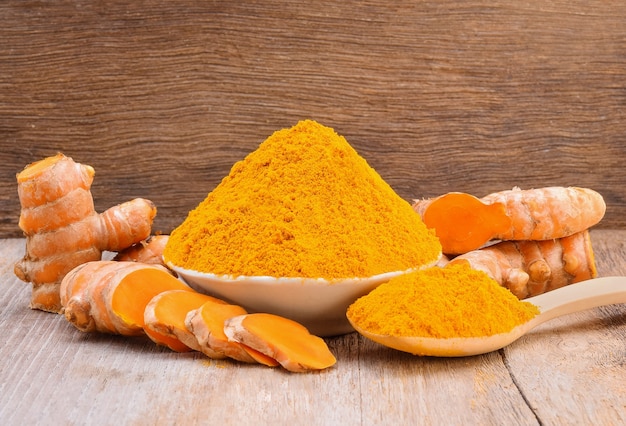 Turmeric roots with turmeric powder on wooden background