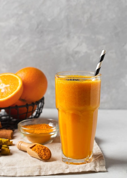 Turmeric smoothie in glass with ingredients powder ginger and spice on white or light grey background