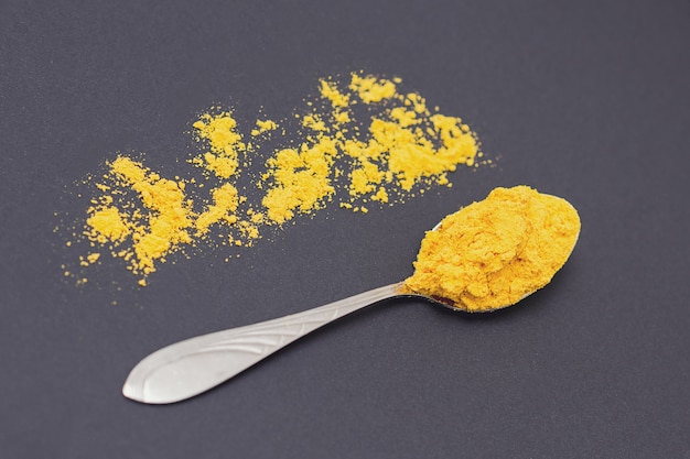 Turmeric spice on a metal spoon on black table.