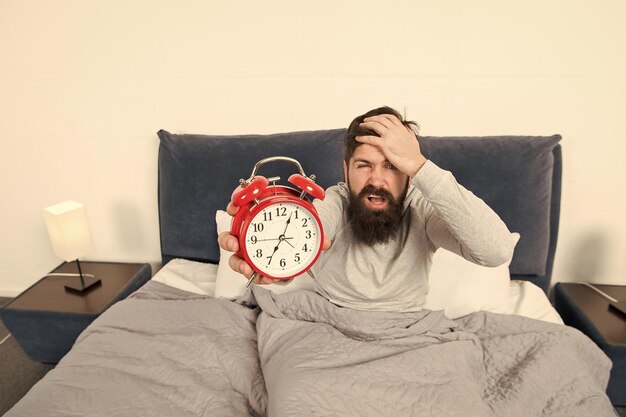 Turn off that ringing Problem early morning awakening Get up with alarm clock Overslept again Tips for waking up early Man bearded sleepy face bed with alarm clock in bed What terrible noise