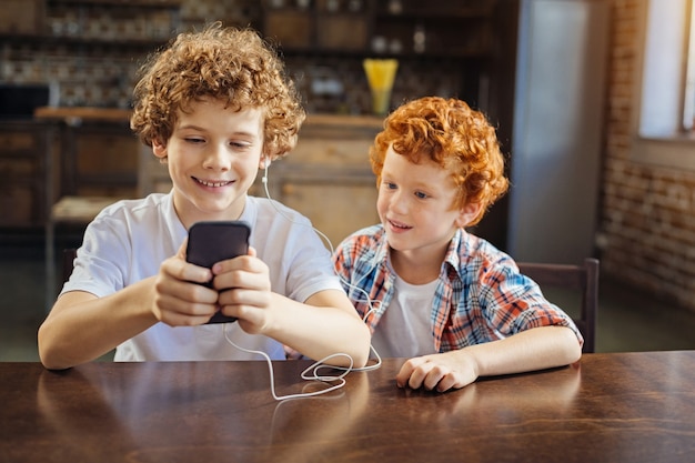 Accendi questo. adorabile ripresa di due bambini di età diversa seduti uno accanto all'altro e concentrando la loro attenzione sullo schermo di uno smartphone mentre entrambi ascoltano la musica a casa.