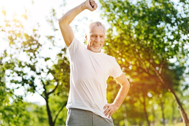 Turn this way. Overjoyed smiling aged man doing sport exercises