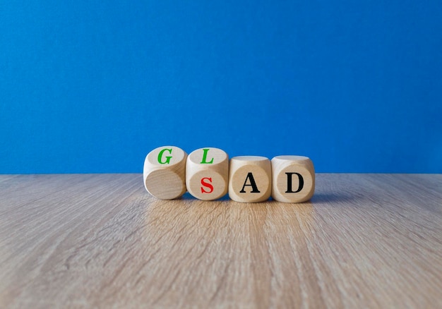 Turned wooden cubes and changes red words Sad to Glad Beautiful blue background wooden table Copy space Business motivational and glad or sad concept