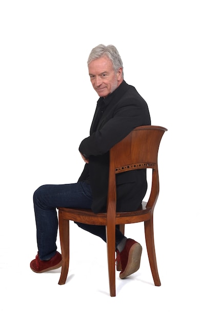 Photo turnig around of a man sitting on chair with sneakers jeans and blazer on white background