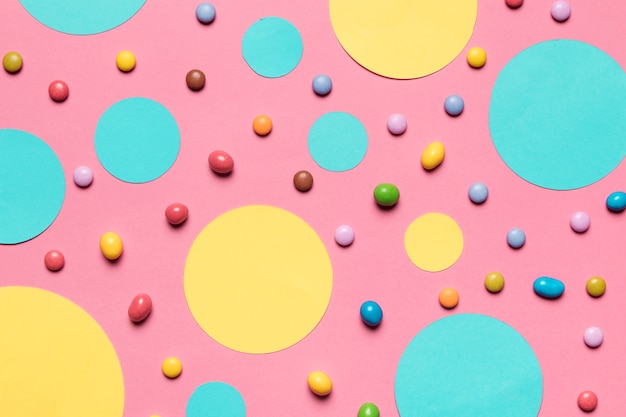 Фото Бирюзовые и желтые круглые рамки с разноцветными конфетами на розовом фоне
